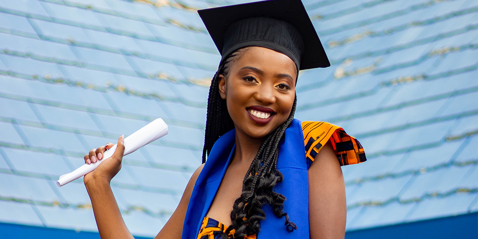 Woman with graduation cap is holding a diploma in her right hand and smiling.